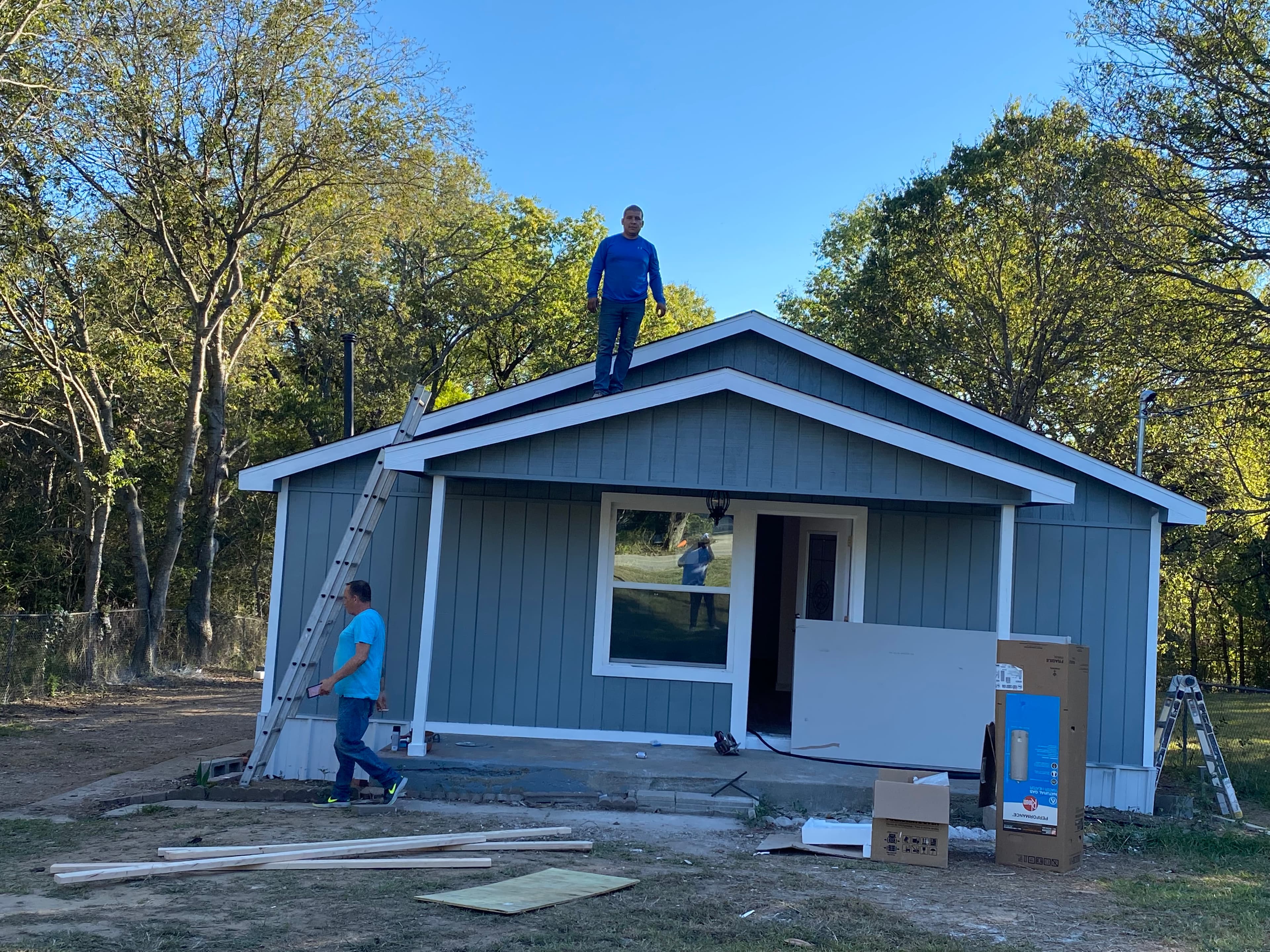 Two men working on a grey house with white trim, one standing on the roof.